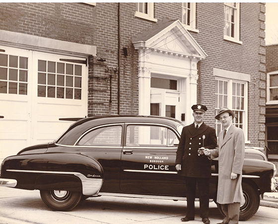 A classic black police car parked outside a historic brick building