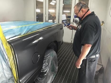 A technician wearing safety gear spray-painting the rear side of a black car inside a paint booth